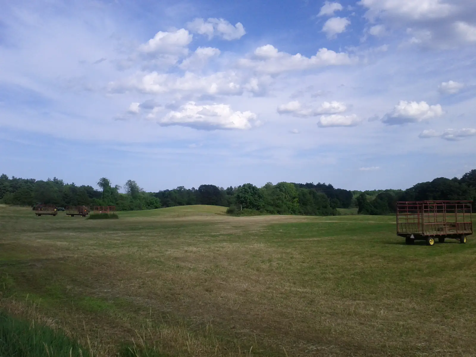 An open hayfield with a hay wagon under a wide summer sky on a farm in Dracut, Massachusetts