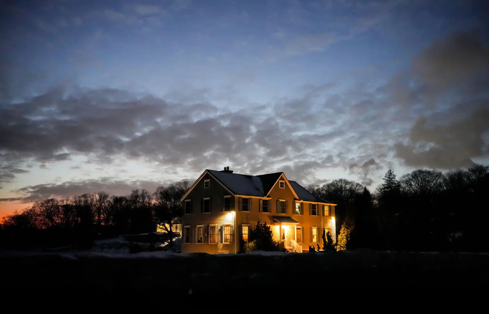A two-story colonial house with glowing windows under a dramatic twilight sky
