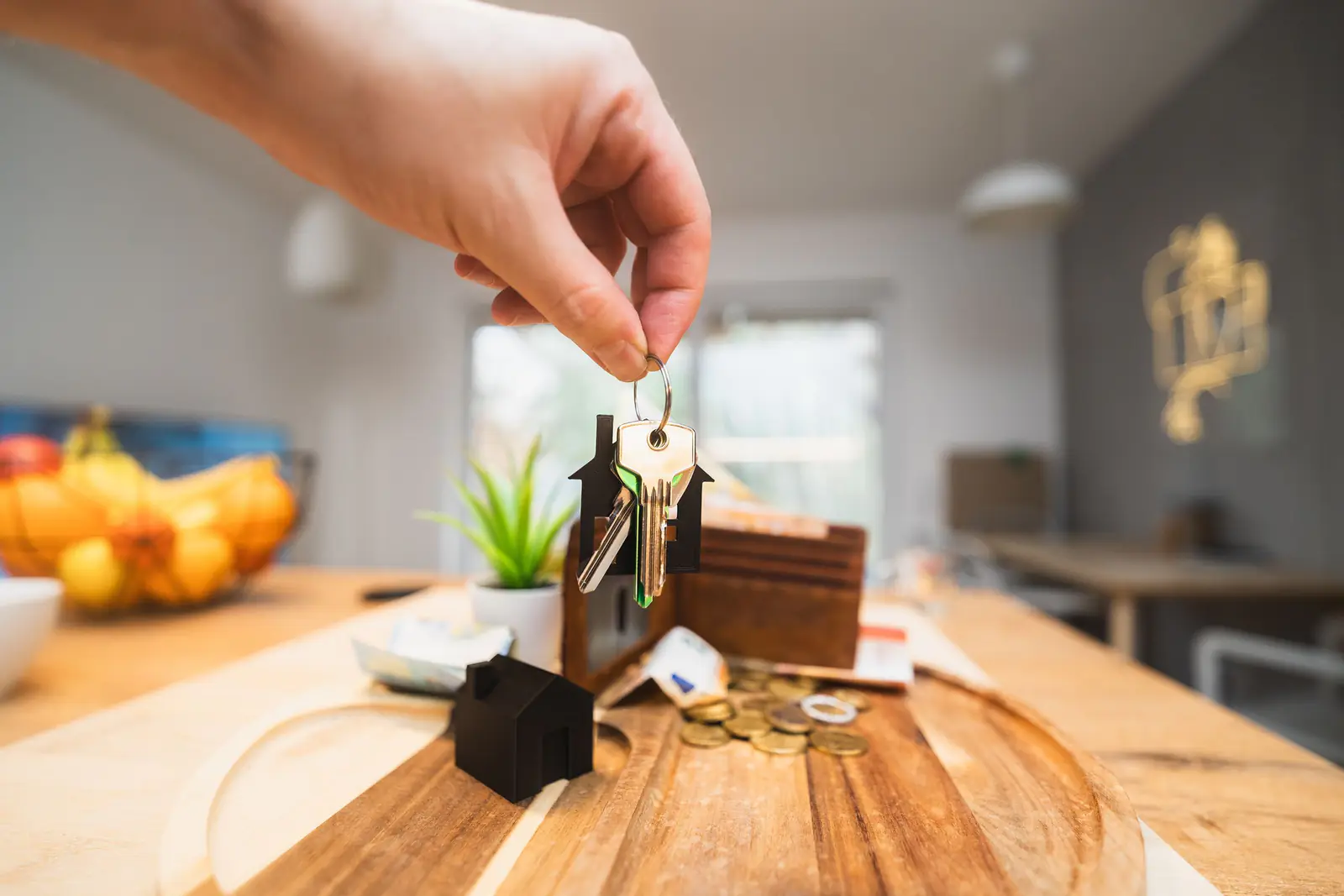 A hand holding house keys with a small house keychain above a table in a new home