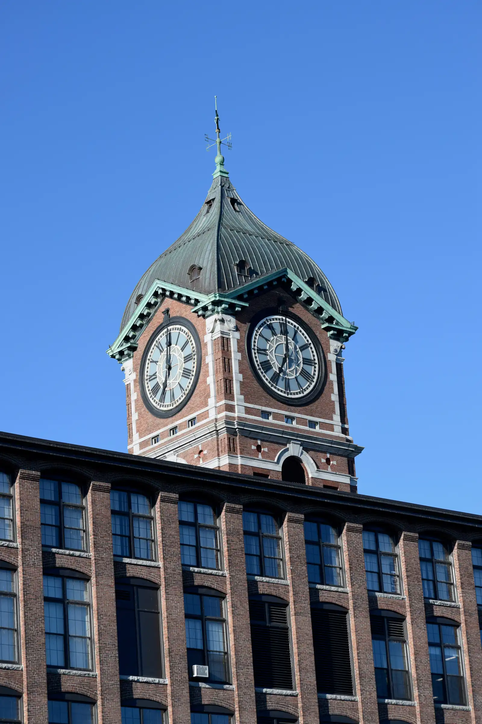 The Ayer Mill clock tower rising above the brick mill building against a clear blue sky in Lawrence, Massachusetts