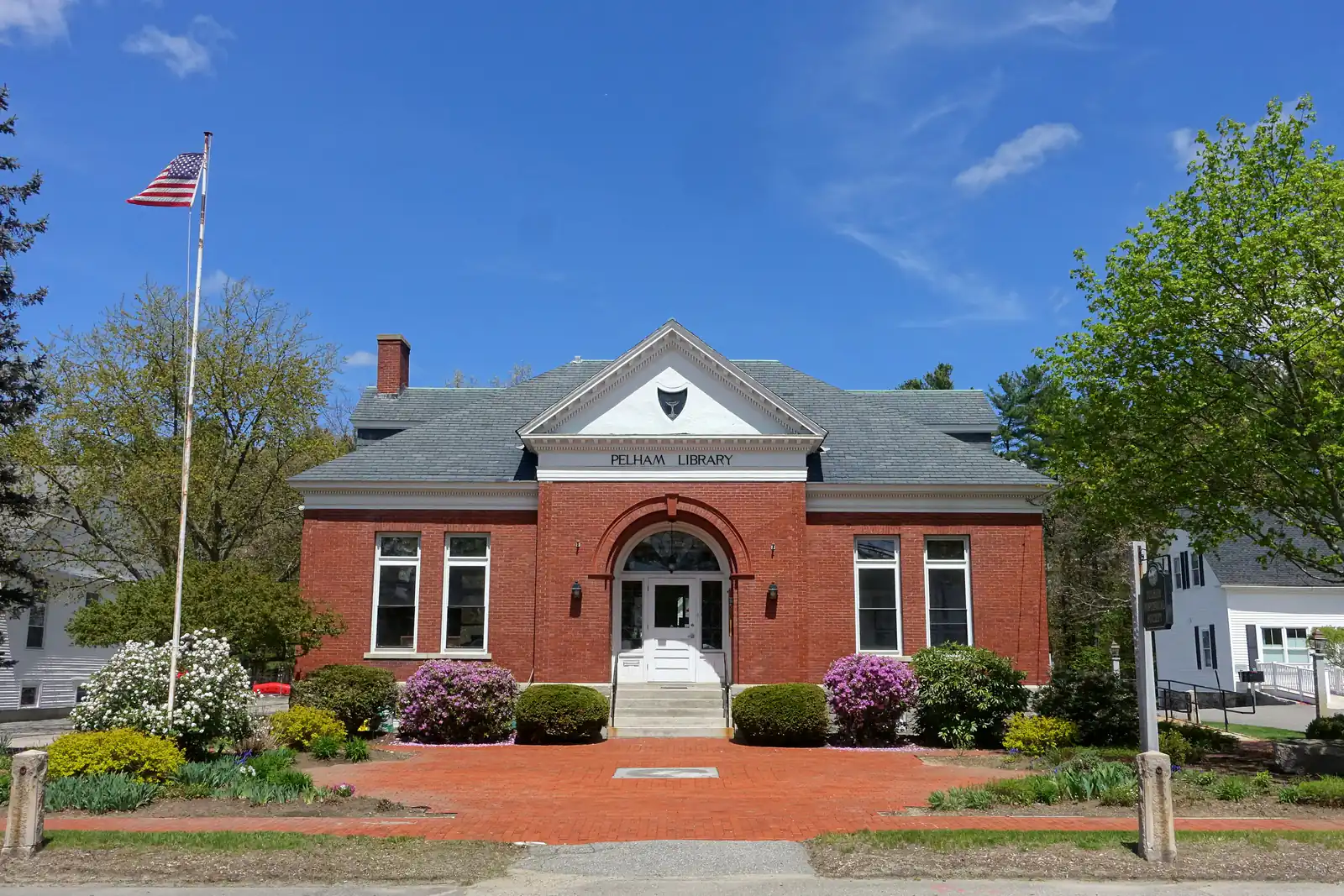 The brick Pelham Library with spring flowers and an American flag in Pelham, New Hampshire